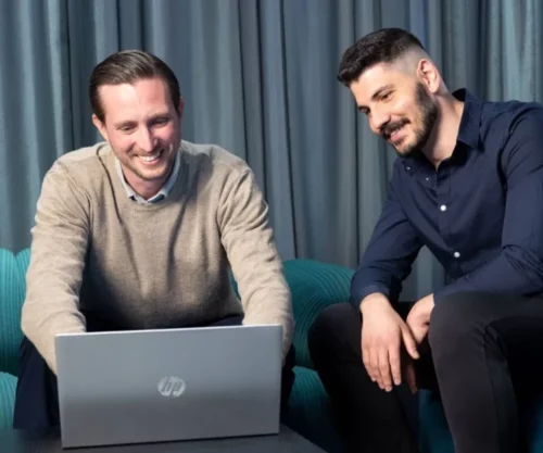 Två personer sitter i en lounge och ler medan de tittar på en laptop. Ett stabilt och säkert Wi-Fi är avgörande för smidig uppkoppling utan krånge
